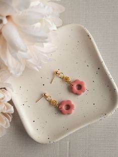 two pink donuts hanging from gold earwires on a white plate next to flowers