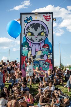 a large group of people sitting on the grass in front of a sign with an image of a cat