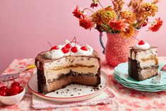 two pieces of cake on plates with cherries and flowers in the vase behind them