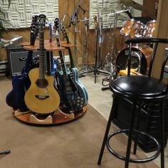 guitars are stacked on top of each other in a room with stools and drum stands