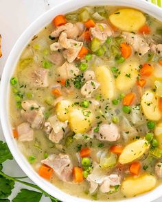 a white bowl filled with chicken, potatoes and carrots next to some parsley