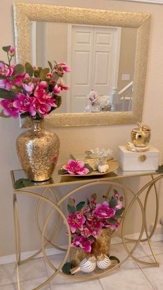 a table with flowers on it in front of a mirror and a vase filled with pink flowers