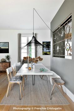 a dining room table and chairs in front of a window with an art piece hanging from the ceiling