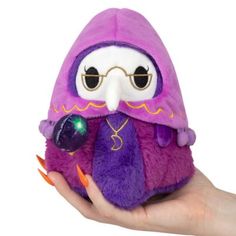 a hand holding a purple stuffed animal with big eyes and an eye patch on it's face