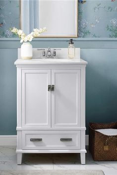 a white bathroom vanity with blue walls and flowers on the mirror over it's sink