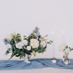 two vases filled with white and blue flowers sitting on top of a blue cloth