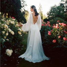 a woman in a white wedding dress standing next to some flowers and bushes with her back turned towards the camera