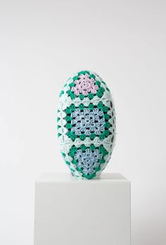 a crocheted easter egg sitting on top of a white pedestal in front of a white wall