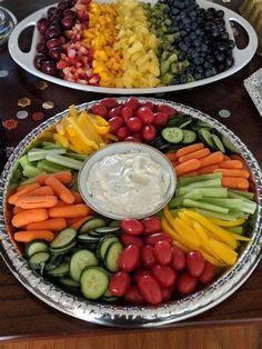 a platter filled with fruit and vegetables on top of a wooden table next to a bowl of dip