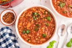 two bowls filled with beans and garnish next to spoons on a table