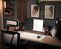 a desk with a computer and speakers on top of it, in front of two framed pictures