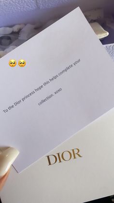 a person holding up a paper with two smiley faces on it and the word dior written in gold