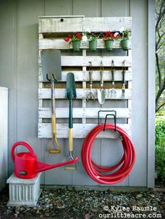 a garden tool rack with gardening tools hanging on it's side wall next to a fire hydrant