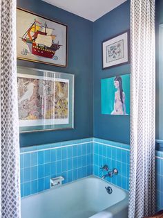 a bathroom with blue tiles and pictures on the wall above the bathtub is shown