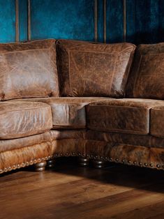 a brown leather sectional sofa with studded arms and foot rests against a blue wall