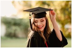 a woman wearing a graduation cap and gown holding her hair in the air with both hands