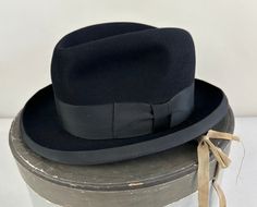 Spruce up any suit with this 1950's Homburg hat! The fur felt is black with a sumptuous feel and a black wide grosgrain ribbon runs around the crown and trims the brim.  It has a leather inner hat band and is fully lined. Made by "Stetson" and comes with its original box! The box shows some wear, but the hat is in excellent vintage condition with no holes, stains, or odors to note.    We didn't find a size tag, but estimate this to be a size 7&1/2 - 7&5/8. Inner circumference: 23.75" Length (at Vintage Black Fedora For Kentucky Derby, Fitted Classic Top Hat For Evening Events, Fitted Classic Top Hat For Evening, Retro Fedora With Short Brim For Formal Events, Retro Fedora With Short Brim For Formal Occasions, Vintage Fitted Top Hat With Flat Bill, Retro Short Brim Fedora For Formal Events, Retro Short Brim Fedora For Formal Occasions, Vintage Black Top Hat For Formal Occasions