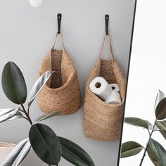 two baskets hanging on the wall next to a mirror with toilet paper and rolls in them