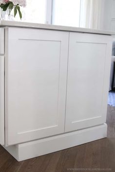 a white cabinet with flowers in it on top of a hard wood floor next to a window