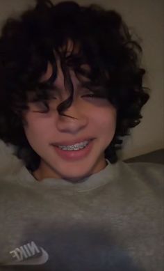 a close up of a person with curly hair wearing a nike shirt and smiling at the camera