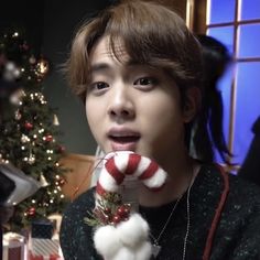 a young man holding a candy cane in front of a christmas tree