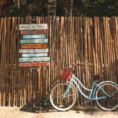 a blue bicycle parked next to a wooden fence with signs on the side and palm trees in the background