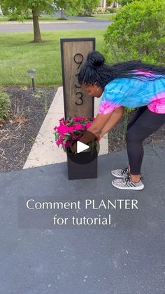 a woman placing flowers in a planter next to a sign