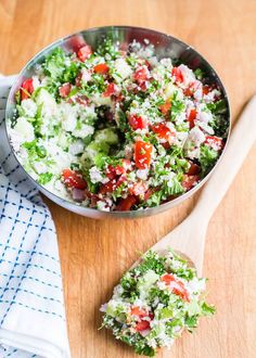 a metal bowl filled with salad on top of a wooden table next to a white and blue towel