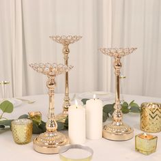 two candles are sitting next to each other on a white table cloth with greenery