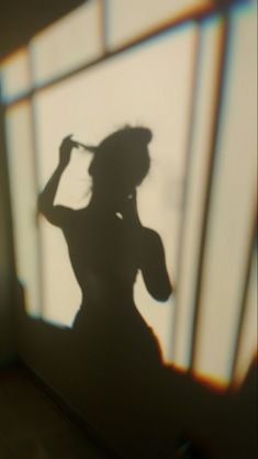 the shadow of a woman standing in front of a window with her hair pulled back