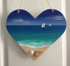 a heart shaped sign hanging on the side of a door with sailboats in the ocean