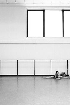 black and white photograph of two people laying on the floor in an empty room with windows