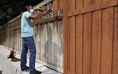 a man using a power drill on a wooden fence with tarp covering the sides