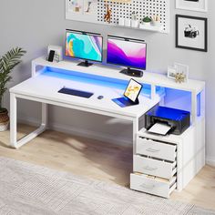 a computer desk with two monitors and a printer on it, in front of a white wall