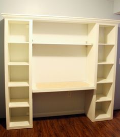 an empty white bookcase with shelves on the wall and wood flooring in front of it