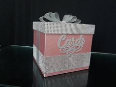 a pink and white gift box sitting on top of a black table next to flowers