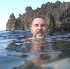 a man swimming in the ocean next to some rocks and water with his eyes closed