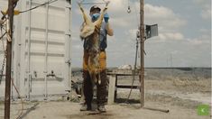 a man holding up a dead animal in front of a white container with other animals