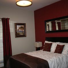 a bedroom with red walls and white bedding, two framed pictures on the wall