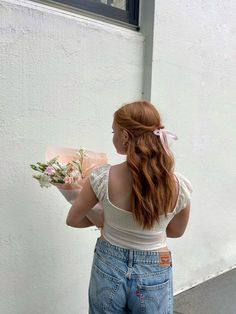 a woman with red hair is holding flowers and looking at the side of a building