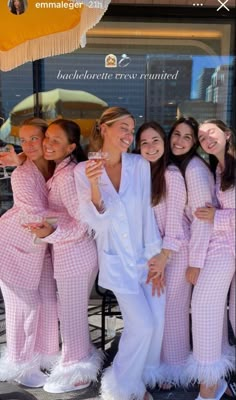 a group of women dressed in pink and white pajamas posing for a photo with an umbrella