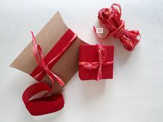 red ribbon wrapped in brown paper and tied with twine on white surface next to gift box