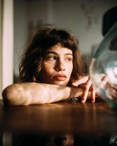 a woman sitting at a table with her hand on top of the glass vase in front of her