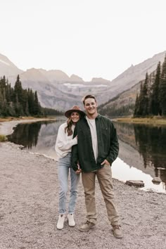 a man and woman standing next to each other in front of a lake surrounded by mountains