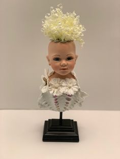 a small doll with blonde hair on top of a black base and white ruffled dress