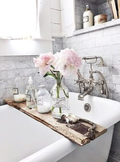 a white bath tub sitting next to a window with pink flowers in vases on it