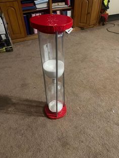 a red and white container sitting on top of a carpeted floor next to a book shelf