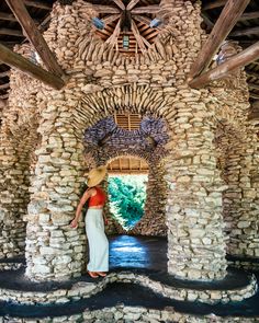 a woman in a straw hat is standing near some rocks and stone pillars that are stacked high into the ceiling