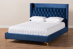 a blue upholstered bed with white sheets and pillows on top of it in a room