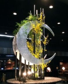 a large metal sculpture with plants growing out of it's sides and the moon on top